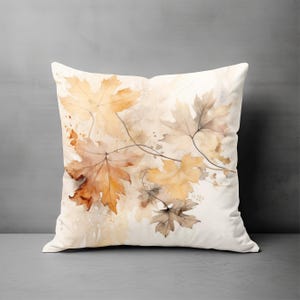 May include: A square throw pillow featuring a watercolor-style print of autumn maple leaves in shades of golden yellow, burnt orange, and soft brown against a cream-colored background. The design includes delicate, thin dark brown stems.