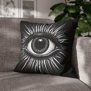 May include: Black and white throw pillow with a graphic design of a large eye with radiating lines. The eye is detailed with a white iris and pupil.