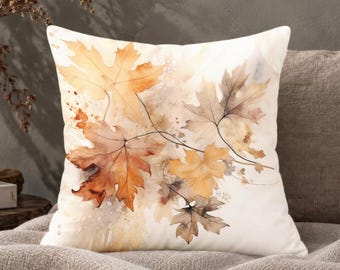 May include: A square throw pillow featuring a watercolor illustration of autumn maple leaves in shades of orange, gold, and brown against a cream-colored background. The design includes delicate leaf veins and soft paint splatters.