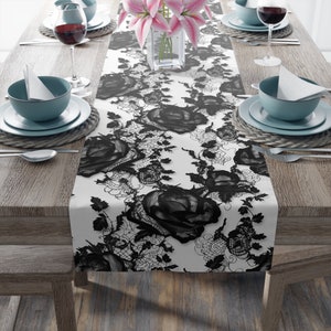 May include: Black and white lace table runner with a floral design. The runner features a repeating pattern of roses and leaves.
