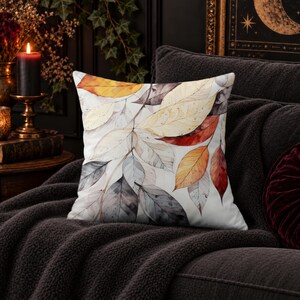 May include: A square throw pillow featuring a watercolor-style print of overlapping autumn leaves in shades of orange, red, yellow, and grey against a white background. The design displays detailed leaf veins and soft, blended color washes.