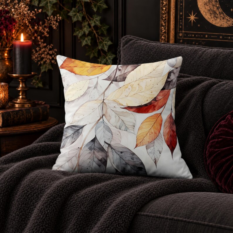 May include: A square throw pillow featuring a watercolor-style print of overlapping autumn leaves in shades of orange, red, yellow, and grey against a white background. The design displays detailed leaf veins and soft, blended color washes.