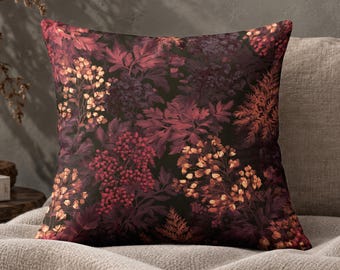 May include: A square throw cushion featuring a dark botanical print with deep burgundy, maroon, and burnt orange floral and foliage patterns against a black background. The design displays clusters of small flowers and fern-like leaves throughout.
