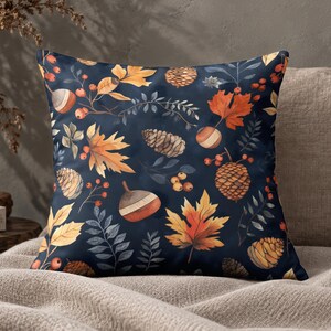 May include: A square throw pillow featuring a dark navy blue background with a repeating pattern of autumn-themed elements including orange and yellow maple leaves, brown pinecones, acorns, and small red berries on thin branches.