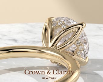 May include: A gold ring featuring a large round faceted centre stone held by a petal-shaped setting with small accent stones along the prongs. The text Crown & Clarity NEW YORK is visible on the band. The ring has a smooth polished finish.