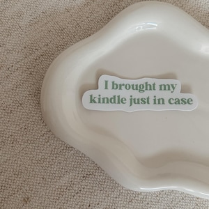 May include: A white ceramic dish with a green sticker that says "I brought my kindle just in case".