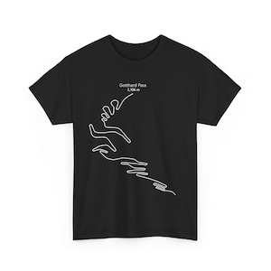 May include: Black t-shirt featuring a white line drawing of a mountain pass. The text "Gotthard Pass 2,106 m" is printed above the design. The shirt is a classic crew neck style.