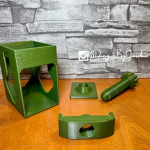 Könnte beinhalten: Grüne 3D-gedruckte Teile, darunter ein quadratischer Halter mit herzförmigen Ausschnitten, eine Basis, ein Gewindeteil und eine zylindrische Komponente. Die Teile sind auf einer Holzoberfläche angeordnet. Der Text "SDesigns By Jordan" ist sichtbar.