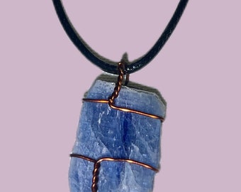 May include: A blue kyanite crystal wrapped in copper wire, hanging from a black cord necklace.