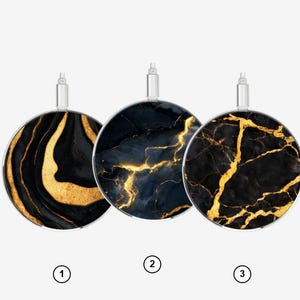 Puede incluir: Tres cargadores inalámbricos circulares con conectores de metal plateado. El primero presenta patrones de remolinos negros y dorados, el segundo muestra vetas azul oscuro y doradas, y el tercero un diseño de mármol negro y dorado.