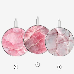 Puede incluir: Tres cargadores inalámbricos circulares con distintos patrones de mármol rosa. Cada cargador tiene un borde metálico plateado y un pequeño conector plateado en la parte superior. Los diseños varían desde texturas cristalinas hasta mármol veteado.