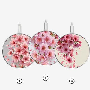 Puede incluir: Tres cargadores inalámbricos circulares, cada uno con un patrón floral de flores de cerezo rosa distinto. Cada cargador tiene un conector de color plateado en la parte superior y está marcado con un pequeño círculo numerado del uno al tres.