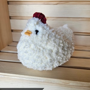 May include: A cream-colored, plush chicken figurine with a red comb and yellow beak. The fluffy, textured body is set against a wooden background. The word "Cream" is displayed in a banner at the bottom of the image.