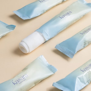 Puede incluir: Un primer plano de una almohadilla de algodón blanco para desmaquillar. La almohadilla está envuelta en un paquete azul y blanco con la palabra "kasara" impresa en él. El paquete está doblado y la almohadilla es visible.