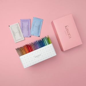 May include: A white box with a pattern of small white squares on a pink background. The box contains a variety of colorful tea sachets. The box is labeled "kasara scents". Three individual tea sachets are visible on the pink background. The sachets are labeled "kasara scents" and are in the colors purple, blue, and white.