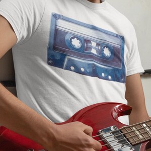 May include: A white t-shirt with a blue and white watercolor illustration of a cassette tape.