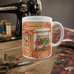 May include: White ceramic mug featuring a whimsical illustration of "The Gingerbread Tailor" shop. The shop's facade is decorated with festive details, including suits, gifts, and a Christmas wreath. The mug is set on a wooden surface with sewing tools.