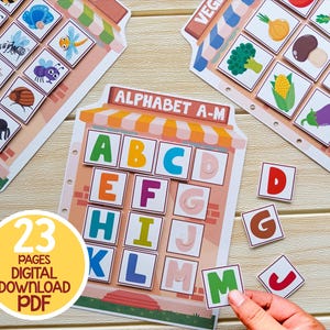 K&ouml;nnte beinhalten: Ein farbenfrohes Alphabet-Lernspiel mit 23 Seiten. Das Spiel zeigt eine Ladenfront mit einem Schild, auf dem "Alphabet A-M" steht. Die Buchstaben A bis M sind in einem Rasterformat dargestellt. Es gibt auch Buchstabenpl&auml;ttchen, die mit den Buchstaben auf dem Spielbrett abgeglichen werden k&ouml;nnen.