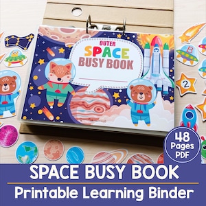 May include: A colourful "Outer Space Busy Book" with a space theme. The cover features cartoon astronauts, planets, and a rocket ship. The book is a printable learning binder with 48 pages. Additional space-themed cutouts are scattered around the book.