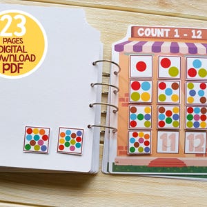 K&ouml;nnte beinhalten: Ein farbenfrohes Z&auml;hlbuch mit 23 Seiten. Das Buch zeigt eine Ladenfront mit einem Schild, auf dem "COUNT 1 - 12" steht. Die Ladenfront hat 12 Quadrate mit verschiedenen farbigen Punkten in jedem Quadrat. Das Buch ist ein digitaler Download im PDF-Format.