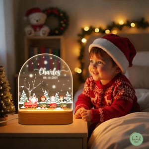May include: A personalized Christmas night light with a wooden base. The clear acrylic panel features a winter scene with a train carrying animals, snowflakes, and the name "Charles" and date "08-16-2025".