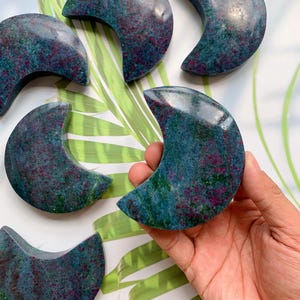 Könnte beinhalten: Eine Sammlung halbmondförmiger Steine mit gesprenkeltem Aussehen. Die Steine weisen eine Mischung aus tiefen Türkis- und Burgunderfarben mit polierter Oberfläche auf. Ein Stein wird in einer Hand gehalten, andere sind verstreut.