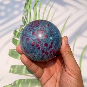 Könnte beinhalten: Eine blaue und rote Edelsteinkugel mit polierter Oberfläche. Die Kugel besteht aus Rubin in Zoisit, auch bekannt als Rubin in Kyanit.