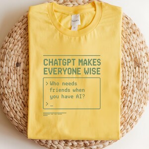 May include: A yellow t-shirt with the text "CHATGPT MAKES EVERYONE WISE" in green pixelated font. Below the text is a simulated text box with the prompt "Who needs friends when you have AI?" The shirt is folded on a woven, circular mat.