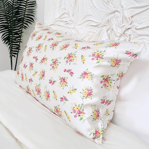 Peut inclure: Une taie d'oreiller blanche avec un motif floral composé de fleurs roses et jaunes. La taie d'oreiller est faite d'un tissu doux et lisse.