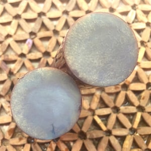 Puede incluir: Dos dilatadores cilíndricos con un acabado iridiscente suave que cambia entre tonos azul suave y dorado pálido. Las caras circulares son planas y pulidas, mostrando un sutil brillo nacarado en la superficie de cada pieza.