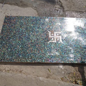 Puede incluir: Una pieza rectangular de incrustación de nácar iridiscente con un diseño de esvástica blanca. La incrustación está hecha de pequeñas piezas irregulares de concha iridiscente.