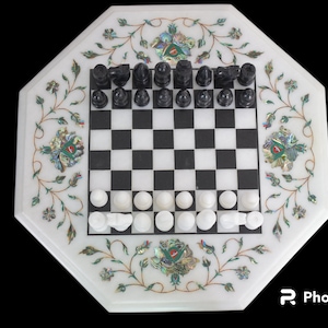 Puede incluir: Un tablero de ajedrez de mármol blanco con intrincados diseños florales incrustados con nácar. El tablero está configurado con piezas de ajedrez blancas y negras.