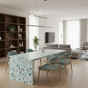 Op de afbeelding: Een moderne eettafel met een terrazzo-achtige oppervlakte in tinten blauw, groen en oranje. De tafel wordt omringd door vier stoelen met licht houten frames en teal-kleurige zittingen. De kamer heeft een houten boekenkast en een neutraal kleurenpalet.