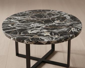 May include: Round coffee table with a black marble top featuring white and gold veining. The table has a black metal base with an X-shaped design. The table is a modern design and sits on a light wood floor.