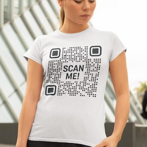 May include: White t-shirt with a black and white QR code that says "SCAN ME!" printed on the front.