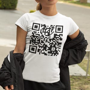 May include: A white t-shirt featuring a black QR code printed on the front. The shirt is being worn by a person wearing sunglasses.