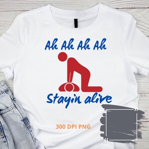 May include: White t-shirt with a red and blue graphic depicting CPR. The text above reads "Ah Ah Ah Ah" in blue, and the text below reads "Stayin alive" in blue. The image also includes "300 DPI PNG".
