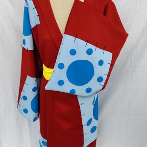 May include: A red and blue patterned kimono with a yellow sash. The kimono has a patchwork design with blue circles on a light blue background.