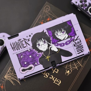 May include: A light purple Nintendo Switch case and controllers featuring anime-style illustrations. The case has the word "HUNTER" in a stylized font, along with character art. The controllers and case have a matching design with a spiderweb theme.