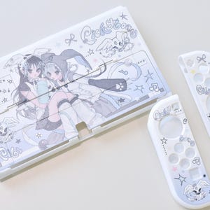 Op de afbeelding: Witte Nintendo Switch-hoes en controller skins met een lichtblauw en grijs anime-achtig ontwerp. De hoes heeft twee anime-personages en de tekst "Cickyboong". De controllers hebben bijpassende graphics.