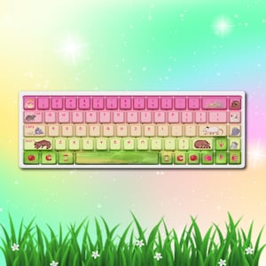 May include: A mechanical keyboard featuring a gradient colour scheme transitioning from pink at the top to green at the bottom. The keys are decorated with various illustrations of small rodents, apples, and hand prints, alongside standard alphanumeric characters.