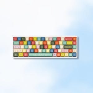May include: A mechanical keyboard featuring a multi-colored layout with red, blue, yellow, green, and cream keys. The keycaps display various icons, including a key, fish, and stars. The text KOWA GAMING STUDIO 2026 is printed at the bottom.