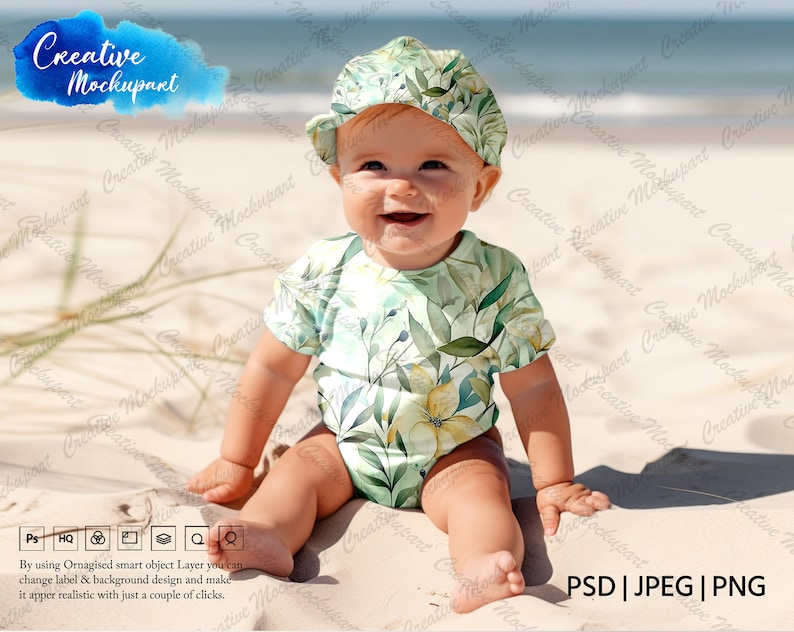 May include: A baby wearing a green and yellow floral print onesie and a green and white floral print hat sits on a sandy beach. The baby is smiling and looking at the camera.