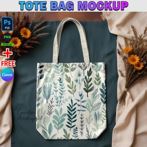 May include: A white tote bag with a green and blue floral pattern. The bag is laying on a blue surface with a beige fabric in the background.