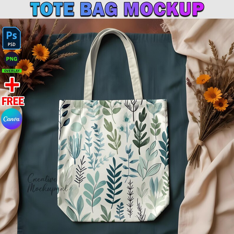 May include: A white tote bag with a green and blue floral pattern. The bag is laying on a blue surface with a beige fabric in the background.