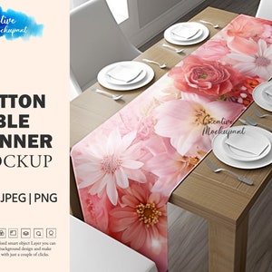 May include: A floral cotton table runner mockup featuring a vibrant design of pink and red flowers. The runner is displayed on a wooden table set with white plates, silverware, and napkins. The text "COTTON TABLE RUNNER MOCKUP" is visible.