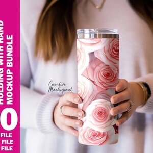 May include: A 20 oz straight tumbler featuring a watercolor design of pink roses. The tumbler is held by a person. The image includes the text: "20 oz TUMBLER STRAIGHT HOLDING WITH HAND MOCKUP BUNDLE", "10", "PSD FILE", "JPEG FILE", and "PNG FILE".