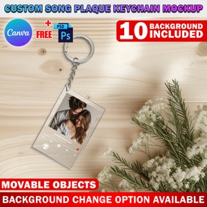 May include: A clear acrylic keychain with a silver metal ring and chain. The keychain features a rectangular plaque with a photo of a couple and a music player interface with play, pause, and skip buttons. The background is a light brown wooden surface with a sprig of white flowers.