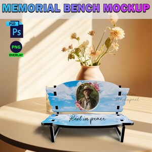May include: A wooden memorial bench mockup with a blue sky and clouds background. The bench has a photo frame with a picture of a man wearing a hat and a floral wreath. The bench has the words "Rest in peace" printed on the front.