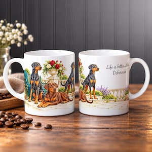 May include: Two white ceramic mugs featuring illustrations of Doberman dogs in a garden setting. One mug shows three Dobermans near a stone planter with flowers, while the other displays a Doberman and the text Life is better with a Doberman.